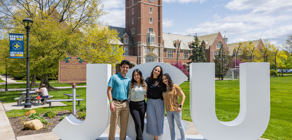 Four students standing close and smiling in front of big letters spelling «Ӱҵ